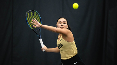 A Purdue women’s tennis player swinging a racquet.